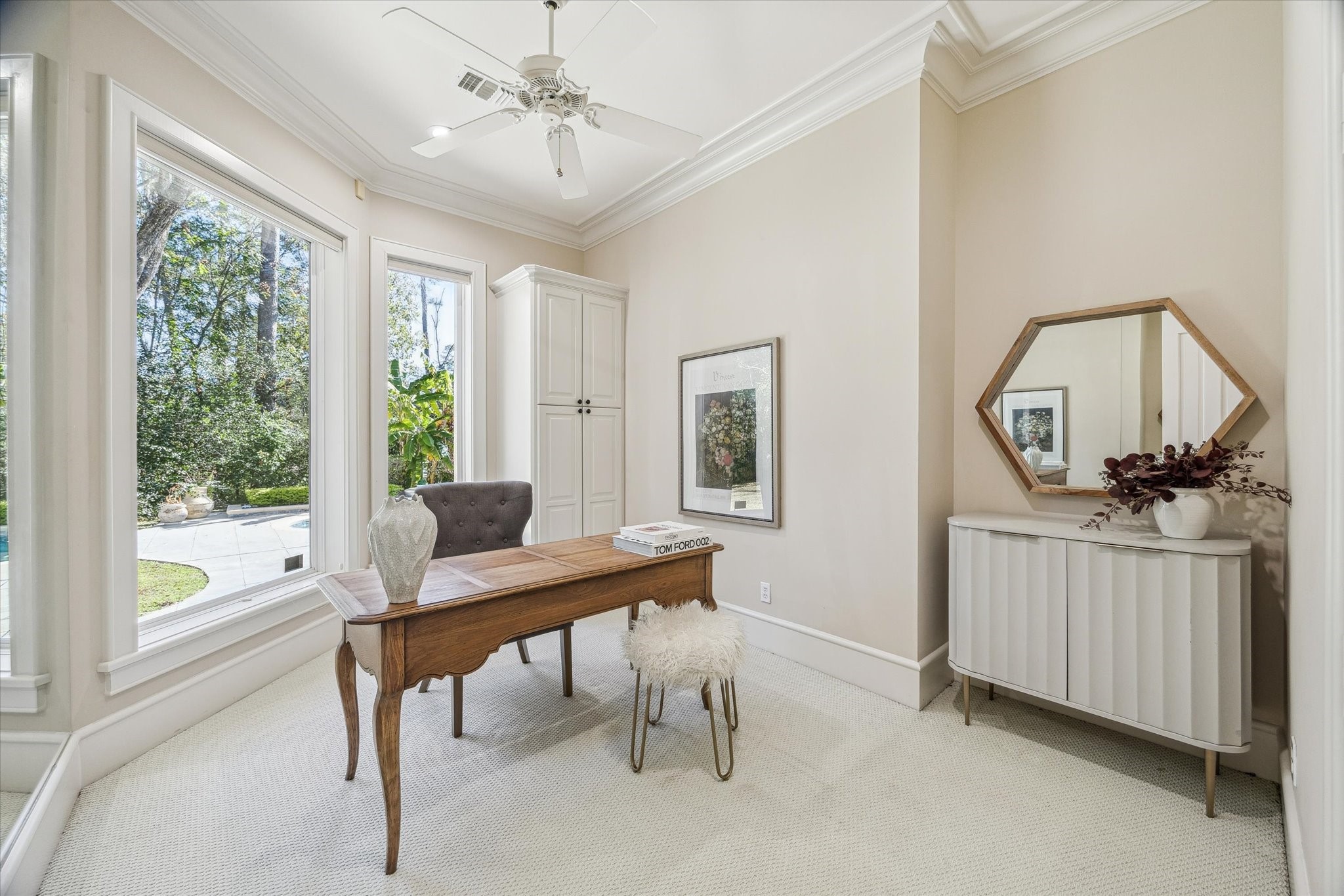 608 Little John Lane Houston, TX 77024 - Photo 24 of 46 This serene secondary office off the primary features neutral carpet flooring and a wall of mirrors that reflect natural light throughout the space. Windows offer peaceful views of the backyard lawn, while a ceiling fan, built-in storage cabinet, and double crown molding provide both functionality and refined detail.