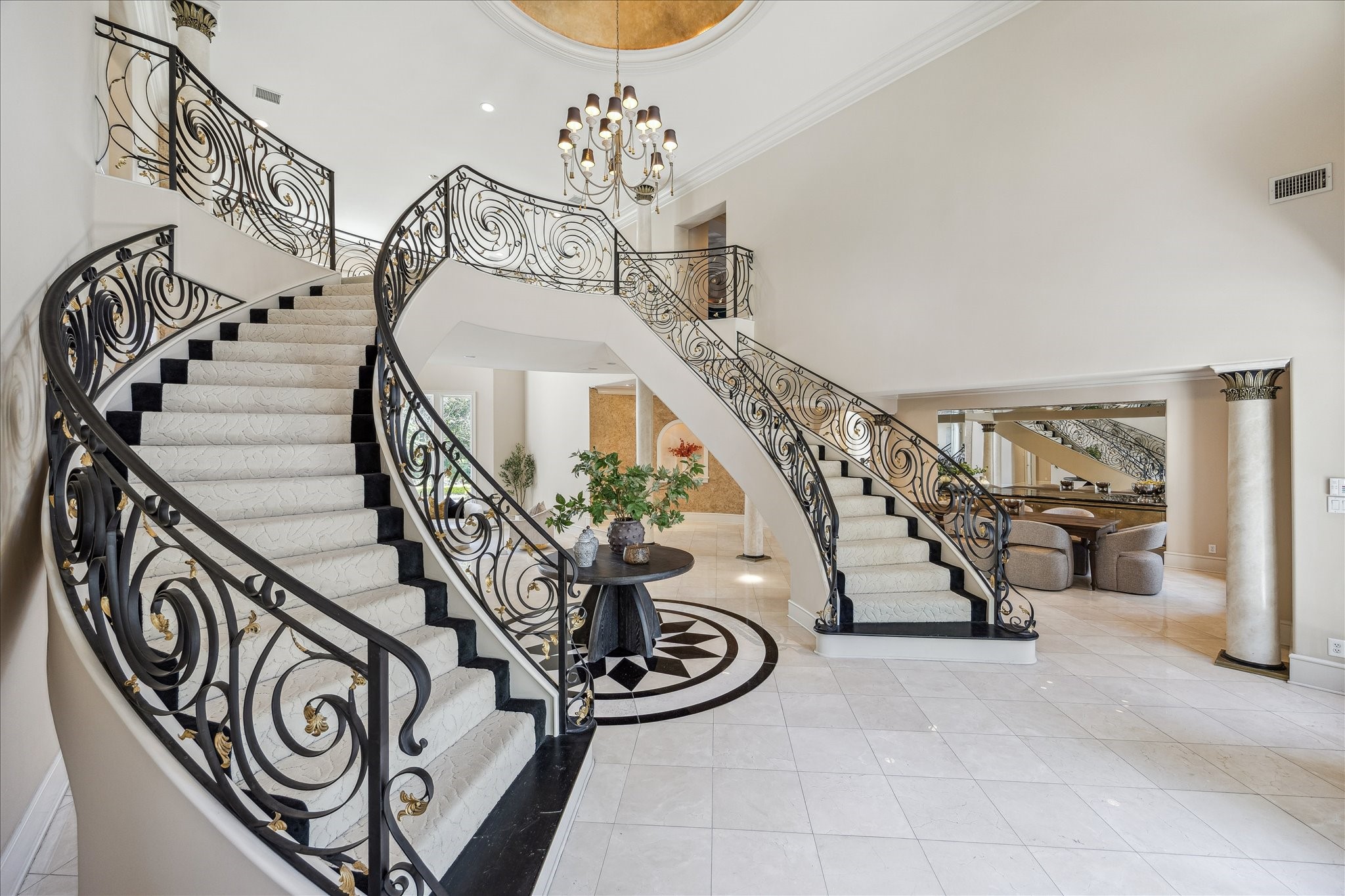 608 Little John Lane Houston, TX 77024 - Photo 31 of 46 The foyer offers seamless access to both the formal dining room and formal living room, highlighted by dramatic west-facing windows. Elegant double curved staircases with a custom stair runner frame the space beneath a double-height ceiling, complemented by polished travertine flooring with a custom medallion inlay. Refined details continue with recessed lighting, granite tile flooring, and thoughtfully designed finishes throughout.