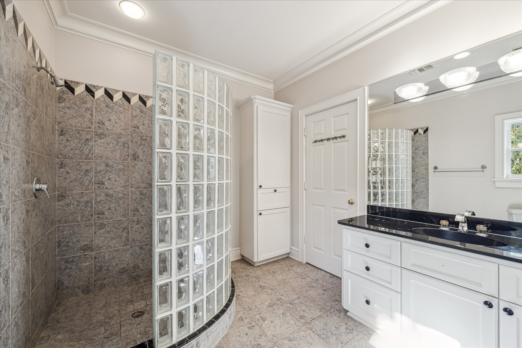608 Little John Lane Houston, TX 77024 - Photo 41 of 46 Guest Bathroom No. 4 features designer neutral wall paint paired with a vanity offering lower cabinetry and drawers. Neutral tile flooring complements a glass block walk-in shower with chrome fixtures, while a window provides southern exposure and natural light.
