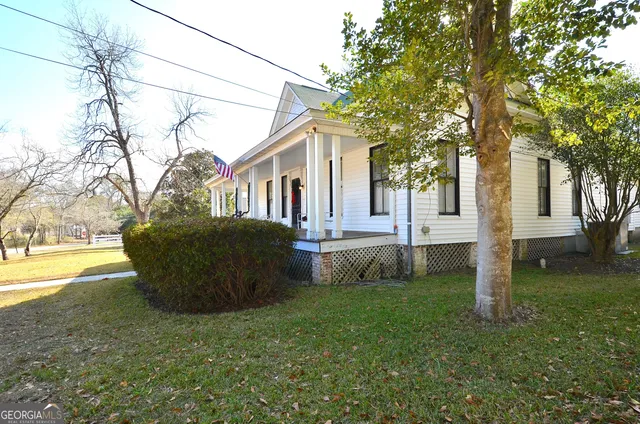 a view of a white house with a large tree and wooden fence