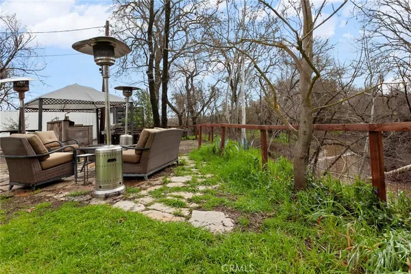 a view of a patio with couches table and chairs under an umbrella with large trees