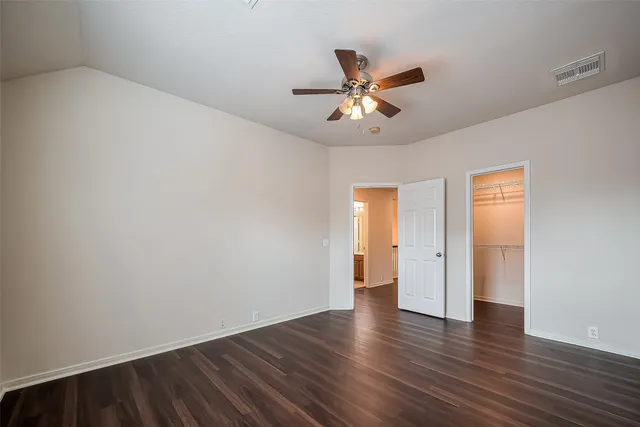 a view of an empty room with wooden floor and a ceiling fan