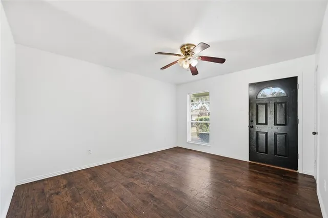 an empty room with wooden floor chandelier fan and windows