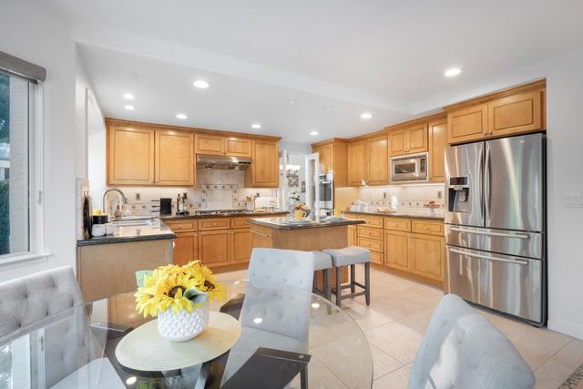 a kitchen with stainless steel appliances granite countertop a refrigerator a sink dishwasher a dining table and chairs with wooden floor