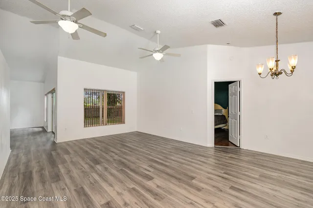 a view of an empty room with wooden floor and a ceiling fan