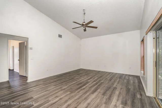 an empty room with wooden floor ceiling fan and windows