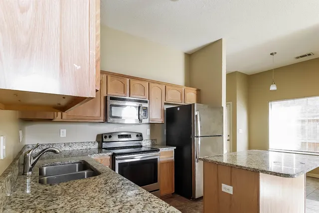 a kitchen with stainless steel appliances granite countertop a refrigerator a stove and a sink with wooden cabinets