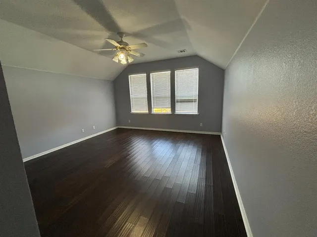 an empty room with wooden floor fan and windows