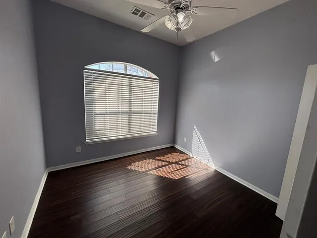 an empty room with wooden floor chandelier fan and windows