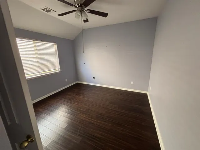 an empty room with wooden floor fan and windows