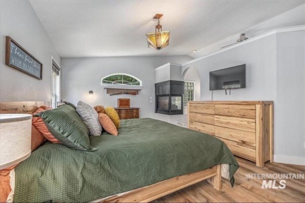 6600 East Victory Road Nampa, ID 83687 - Photo 11 of 19 Spacious sleeping area featuring wood-finish flooring, a corner fireplace with a dark surround, a vaulted ceiling, and an arched transom window