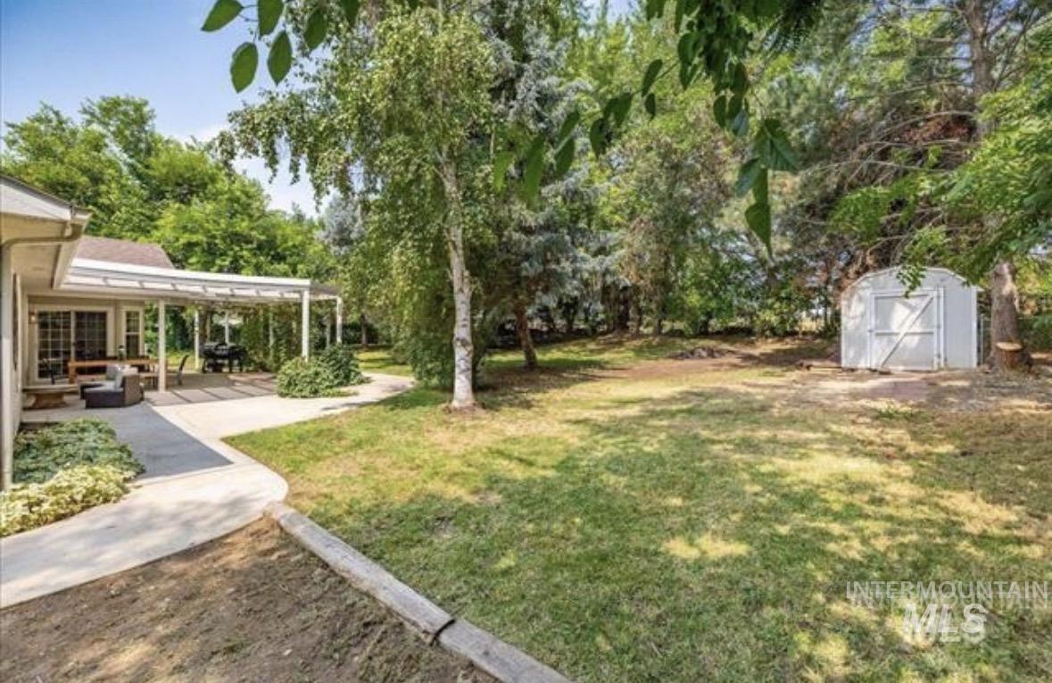 6600 East Victory Road Nampa, ID 83687 - Photo 18 of 19 Expansive backyard featuring a covered patio, mature trees, a storage shed, and a concrete pathway leading from the home