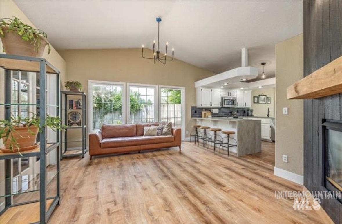 6600 East Victory Road Nampa, ID 83687 - Photo 5 of 19 Spacious living area featuring vaulted ceilings, wood-finish flooring, a kitchen island with seating, a built-in fireplace, and expansive windows