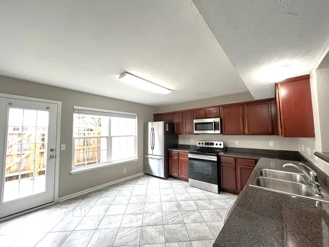 a kitchen with granite countertop a stove top oven a sink dishwasher and a refrigerator with wooden cabinets