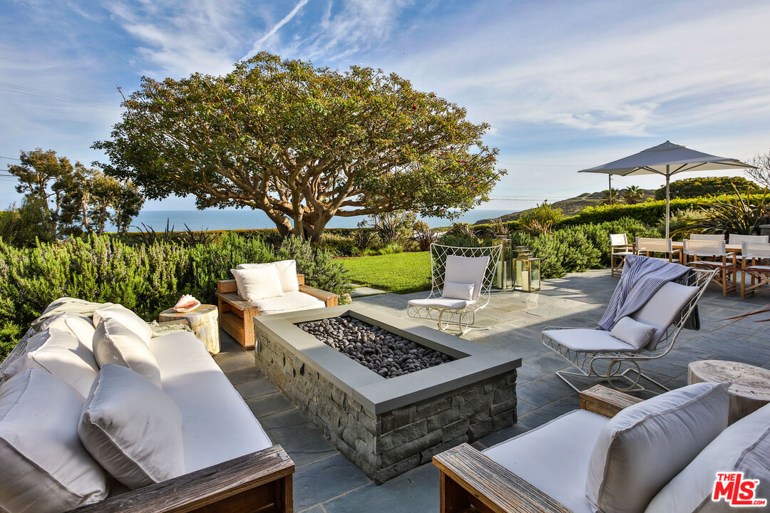 a view of a patio with couches table and chairs under an umbrella with large trees