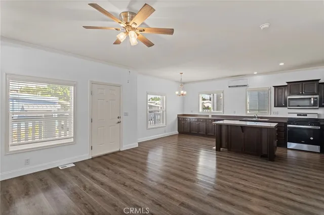 a living room with stainless steel appliances kitchen island granite countertop a stove a refrigerator a sink a microwave oven with cabinets and wooden floor