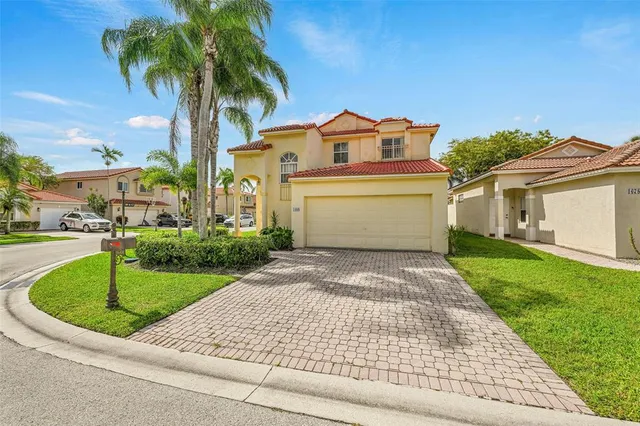 a view of a white house with a big yard plants and palm trees