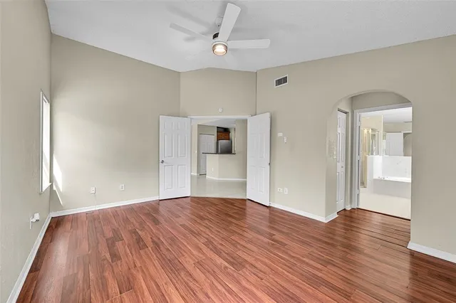 an empty room with wooden floor fan and windows