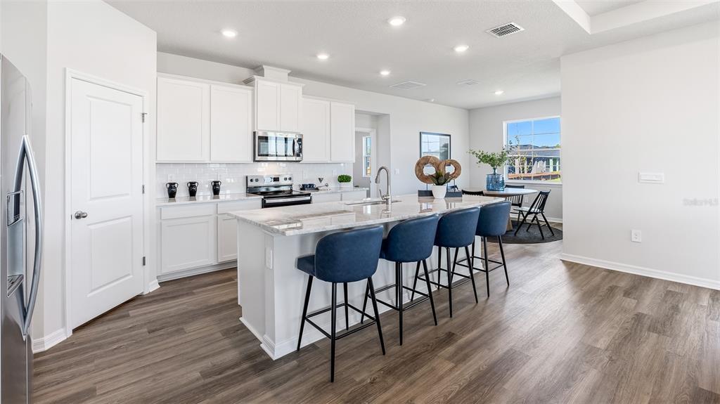 17932 Gander Terrace Lakewood Ranch, FL 34211 - Photo 6 of 52 a kitchen with stainless steel appliances kitchen island granite countertop a table chairs stove and white cabinets