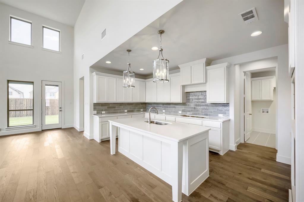 11548 Wulstone Road Haslet, TX 76052 - Photo 7 of 26 Contemporary kitchen featuring white cabinetry, a large center island with a sink, quartz-finish countertops, and a gray subway tile backsplash