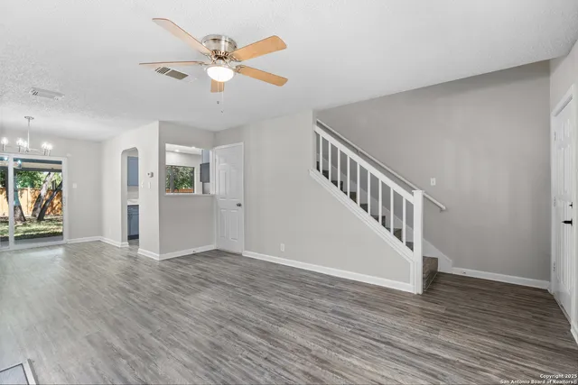a view of an empty room with wooden floor and a ceiling fan