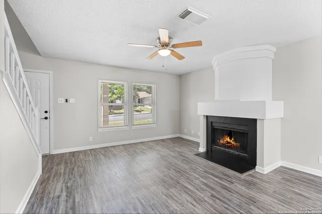 an empty room with wooden floor a fireplace a ceiling fan and a fireplace