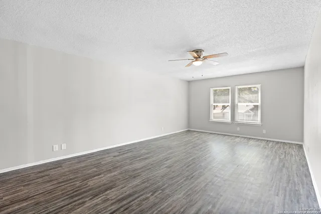 an empty room with wooden floor ceiling fan and windows