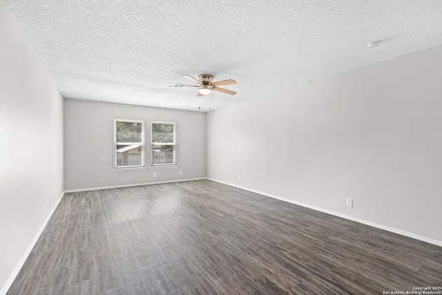 an empty room with wooden floor chandelier fan and windows