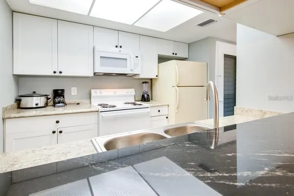 a kitchen with granite countertop a refrigerator and white cabinets