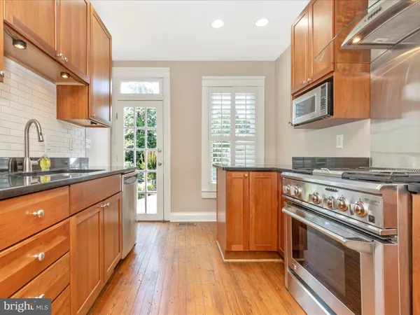 a kitchen with stainless steel appliances kitchen island granite countertop a refrigerator a stove and a wooden floors