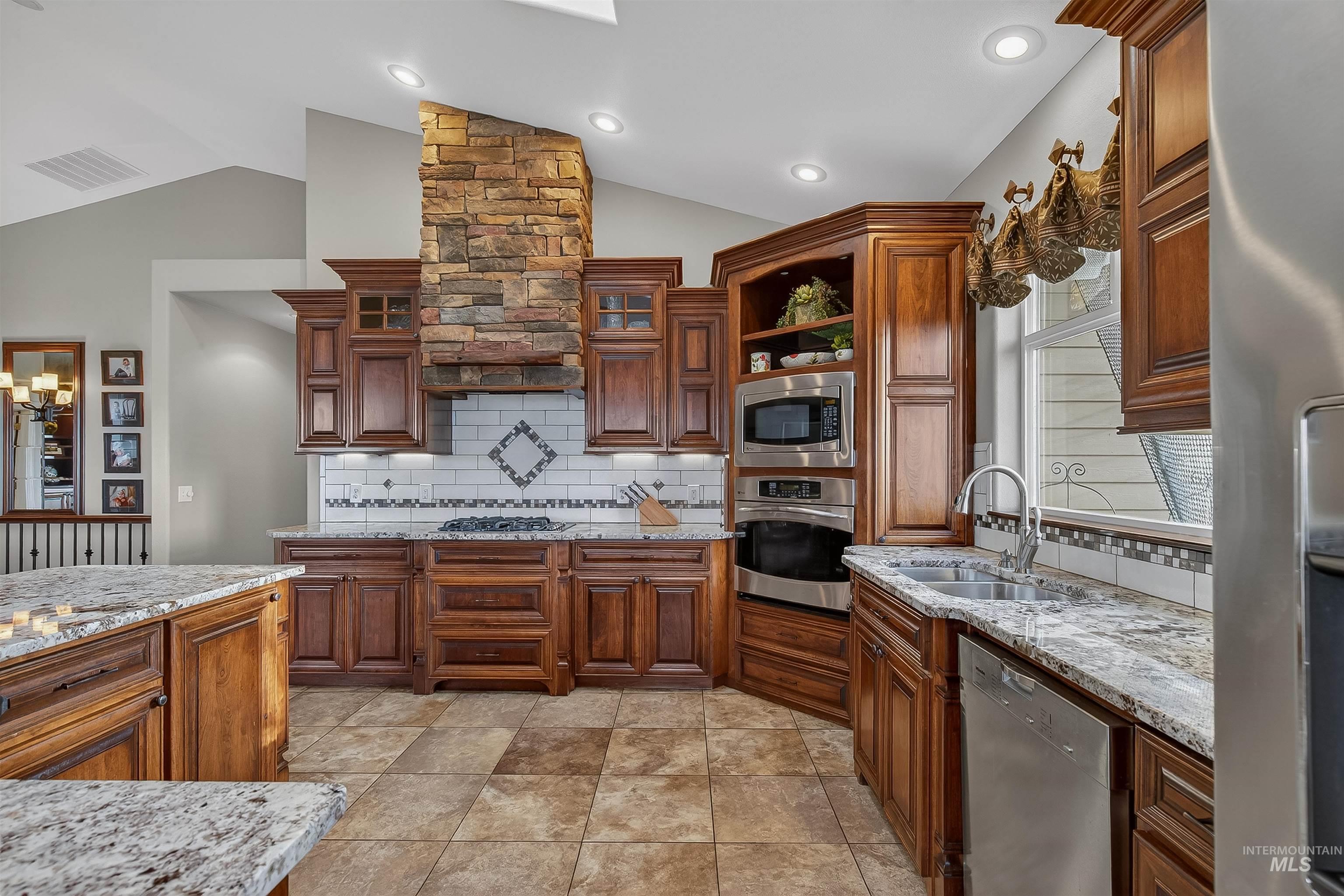 Kitchen with light stone countertops, appliances with stainless steel finishes, open shelves, and lofted ceiling