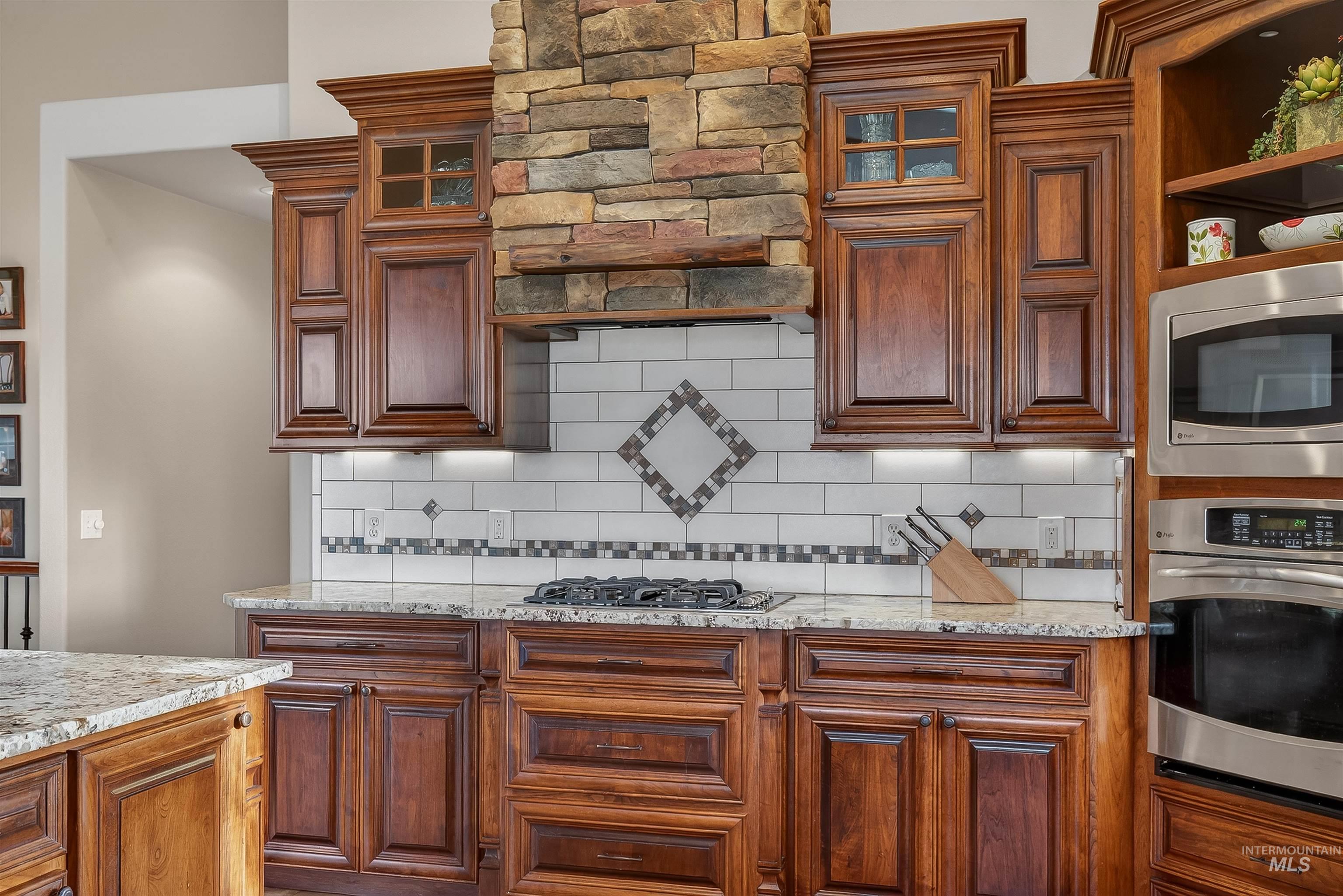 3978 Foothill Drive Lewiston, ID 83501 - Photo 15 of 40 Kitchen with light stone counters, appliances with stainless steel finishes, glass insert cabinets, brown cabinetry, and decorative backsplash