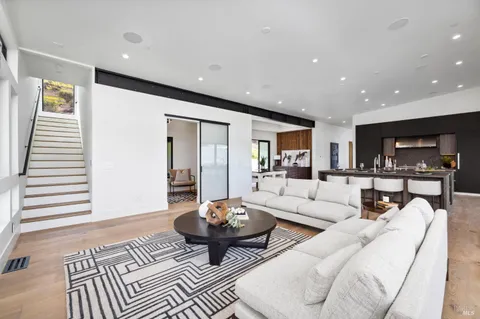 a living room with stainless steel appliances kitchen island granite countertop a refrigerator a sink dishwasher and wooden cabinets with wooden floor