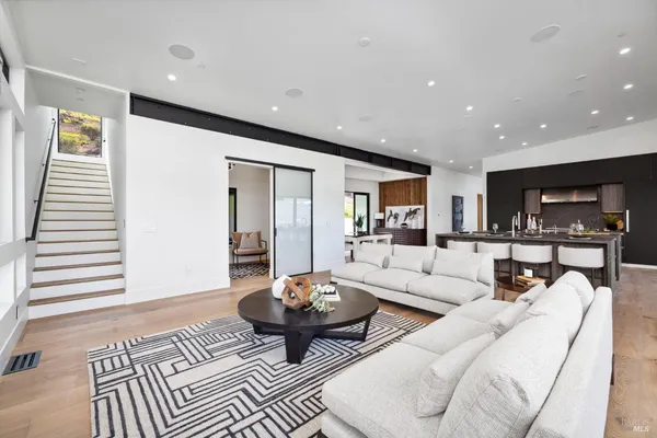 a living room with stainless steel appliances kitchen island granite countertop a refrigerator a sink dishwasher and wooden cabinets with wooden floor