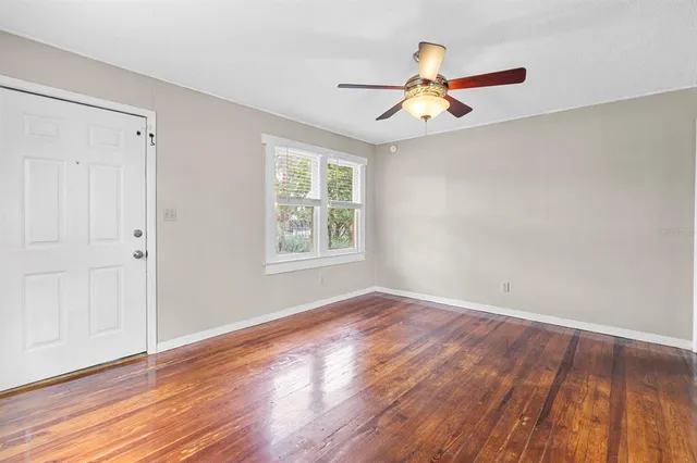 an empty room with wooden floor chandelier fan and windows