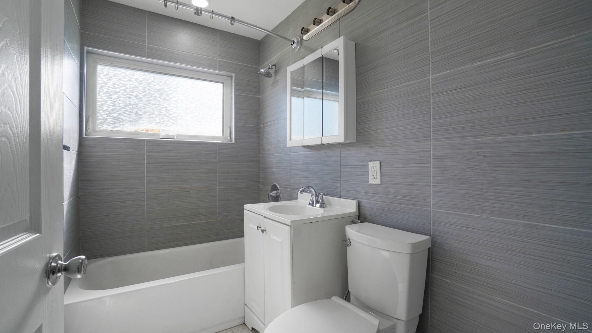 63 Blacksmith Road Levittown, NY 11756 - Photo 14 of 25 Bathroom featuring gray tiled walls, a white bathtub, a single vanity with storage, a mirrored medicine cabinet, and a toilet