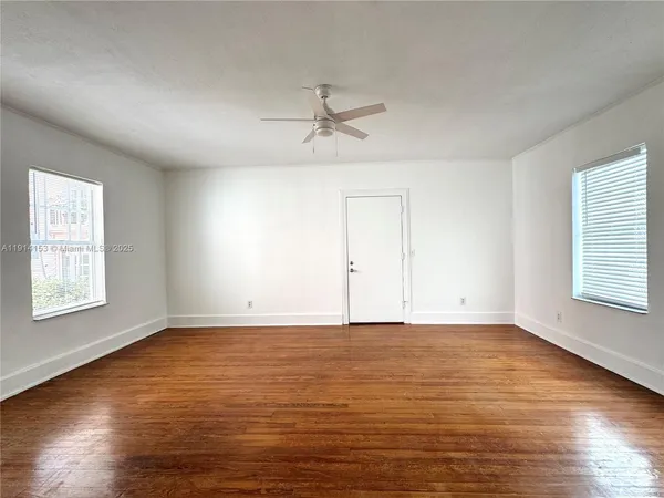 an empty room with wooden floor ceiling fan and windows