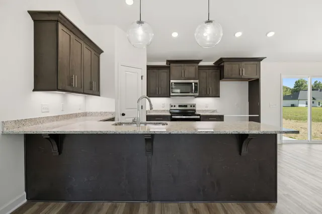 a kitchen with stainless steel appliances granite countertop a sink a stove a refrigerator and island with wooden floor