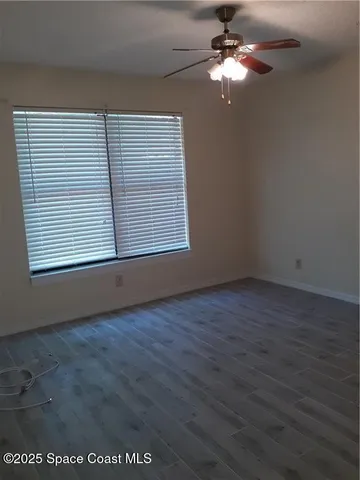 an empty room with wooden floor chandelier fan and windows