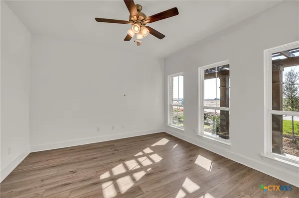 an empty room with wooden floor fan and windows
