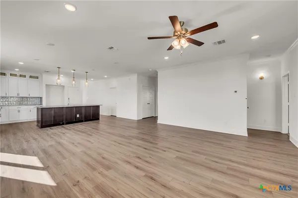 a view of an empty room with wooden floor and a ceiling fan