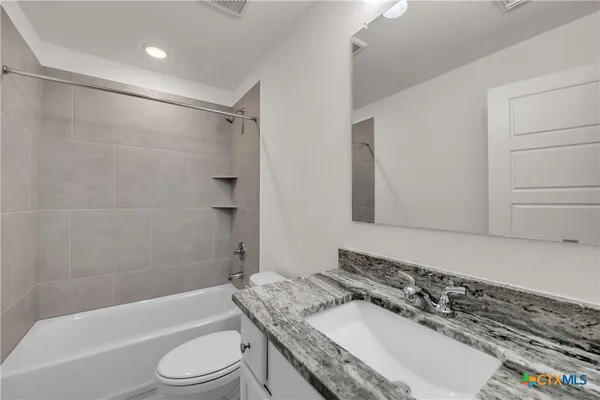 a bathroom with a granite countertop bathtub shower sink vanity and toilet