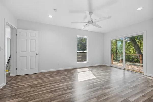 an empty room with wooden floor fan and windows