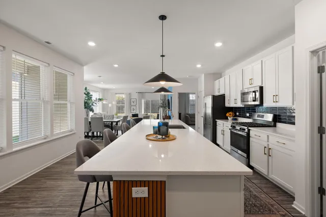 a kitchen with stainless steel appliances kitchen island granite countertop a dining table chairs and white cabinets