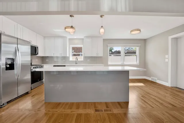 a large kitchen with stainless steel appliances a large counter top a stove a refrigerator and a window