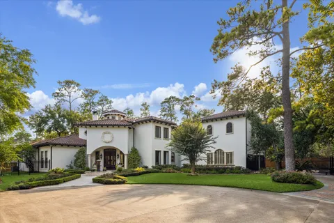a view of a white house with a large tree and flower plants