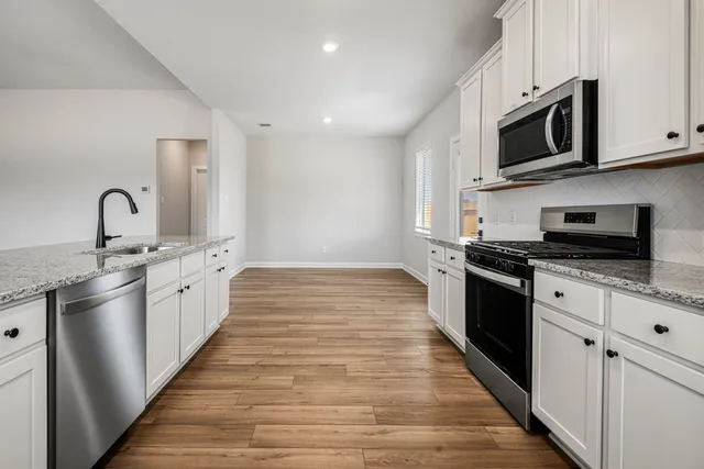 a large kitchen with stainless steel appliances granite countertop a stove top oven a sink dishwasher and white cabinets with wooden floor