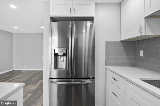 a view of a refrigerator in kitchen and an empty room with wooden floor