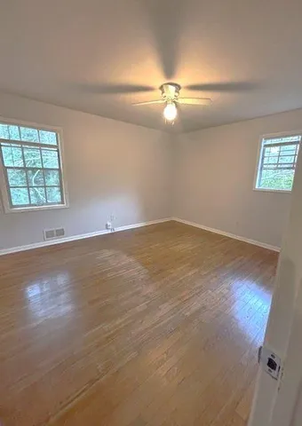 an empty room with wooden floor fan and windows