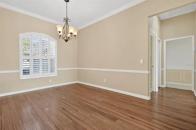 an empty room with wooden floor chandelier and windows